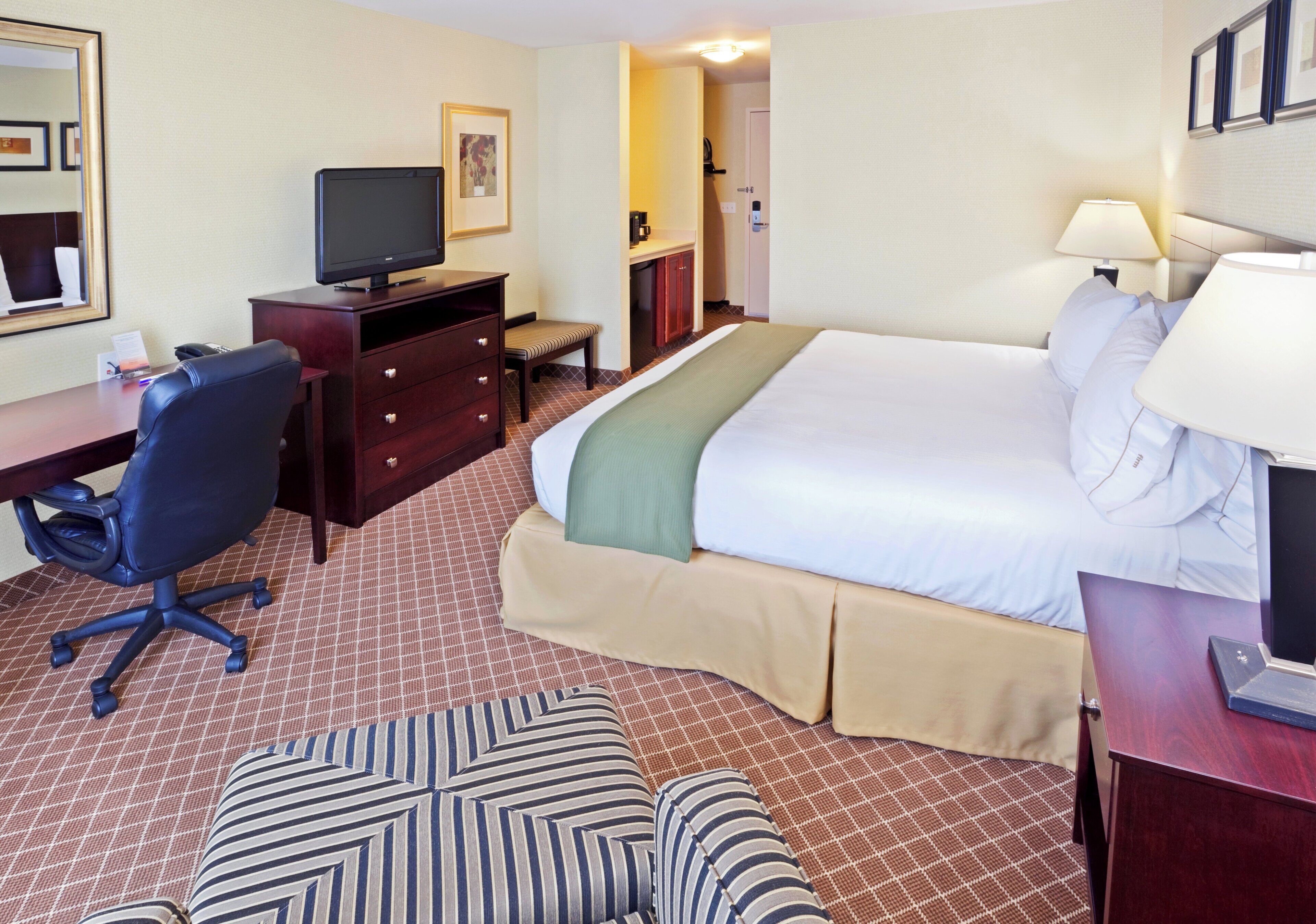 Habitación de hotel con cama, escritorio, silla, televisor, mesita de noche y lámpara.