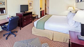 Habitación de hotel con cama, escritorio, silla, televisor, mesita de noche y lámpara.