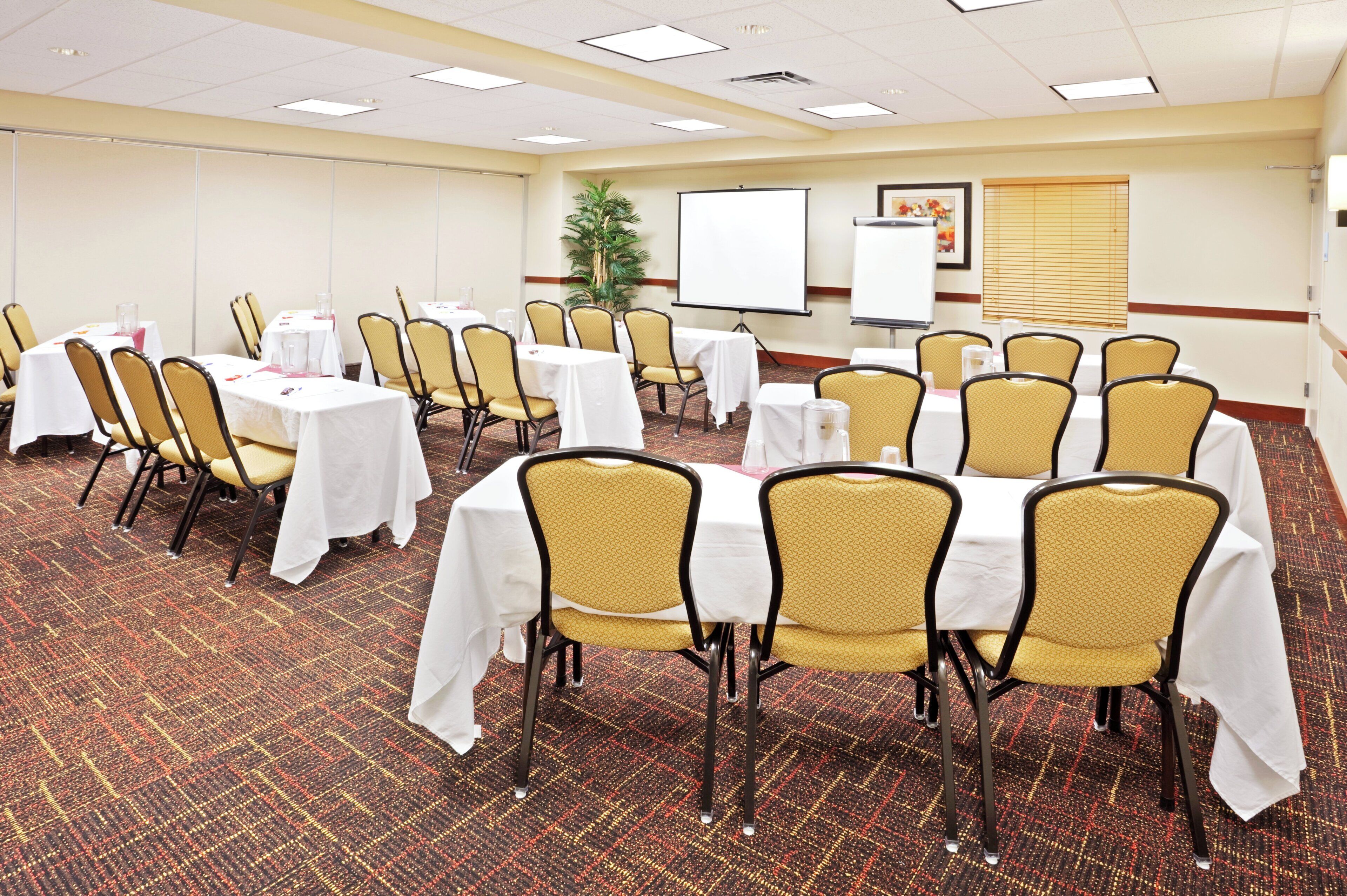 A conference room with tables and chairs, a whiteboard, and a projector screen.
