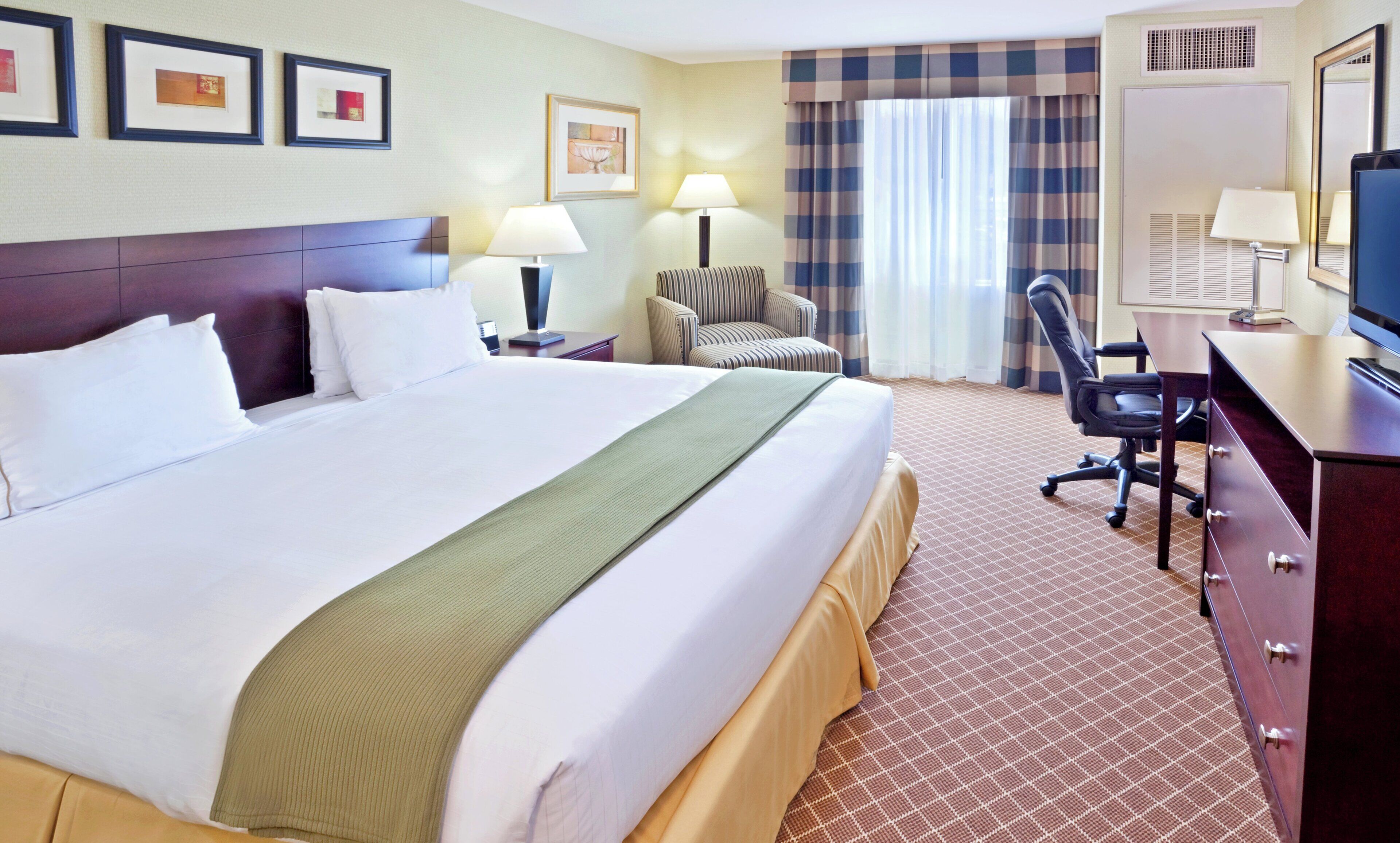 A hotel room with a large bed, a desk, a chair, a lamp, and a television.