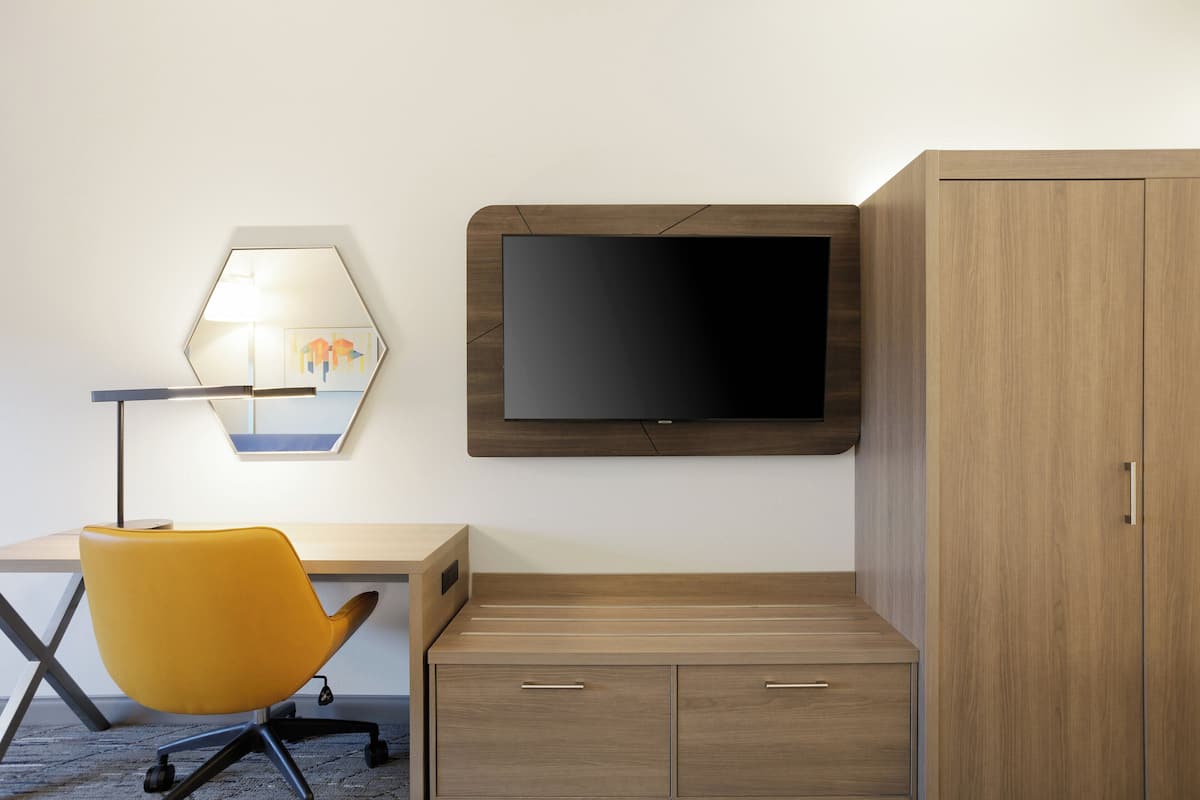 A modern room with a desk, a yellow chair, a mounted TV, and a wooden wardrobe.