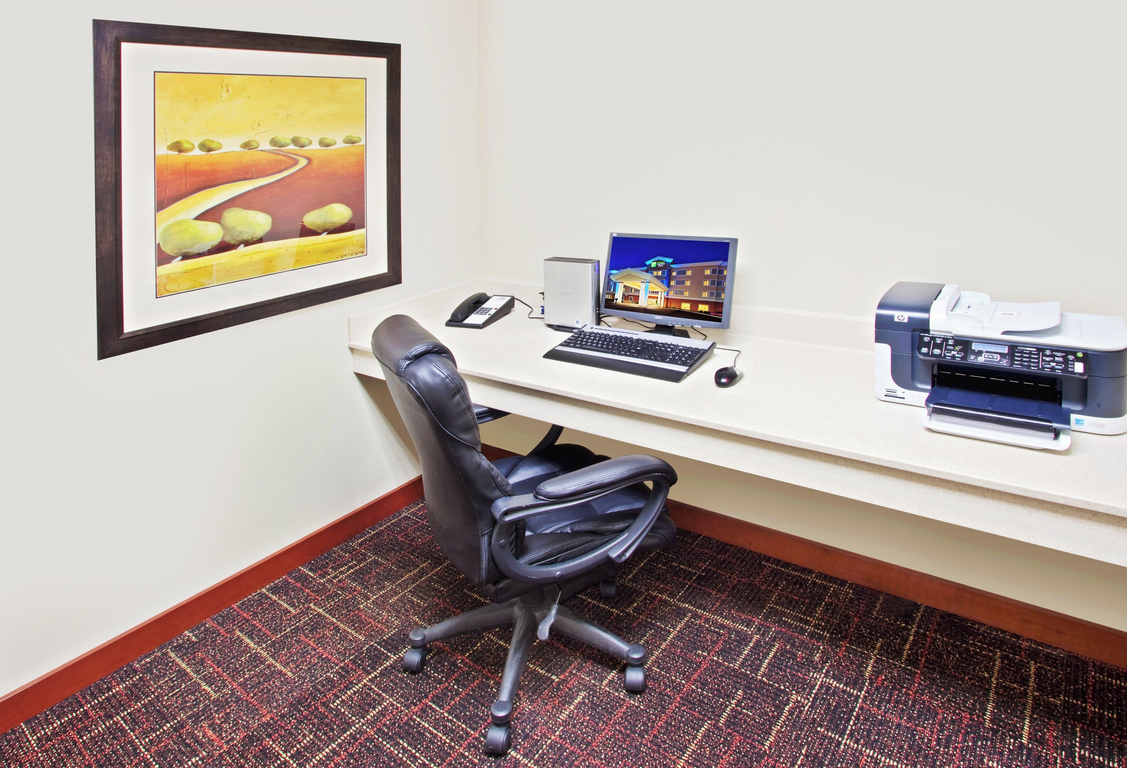 A hotel room with a desk, a computer, a printer, and a telephone.
