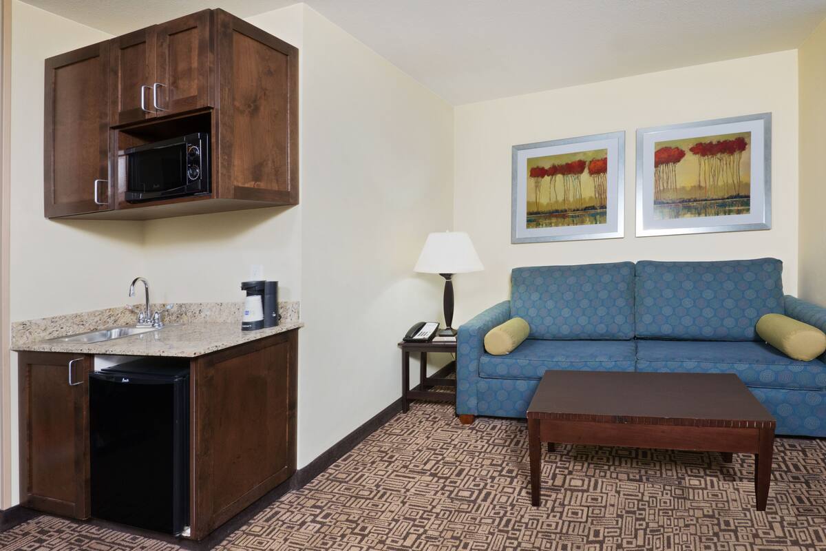 A compact living space with a kitchenette, a blue patterned sofa, a coffee table, and two framed artworks on the wall.