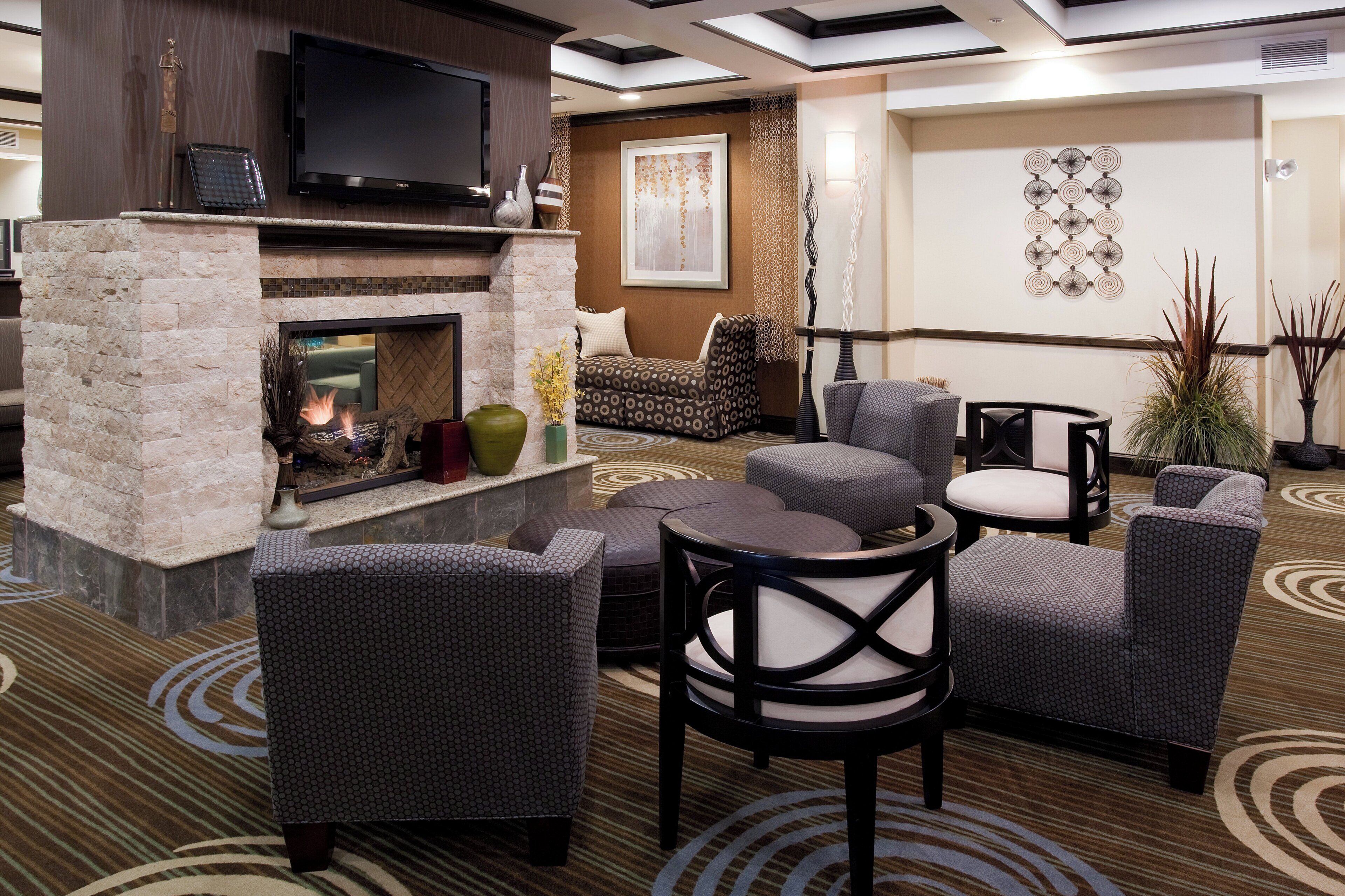 A hotel lobby with a stone fireplace, seating area, and a flat-screen TV mounted above the fireplace.