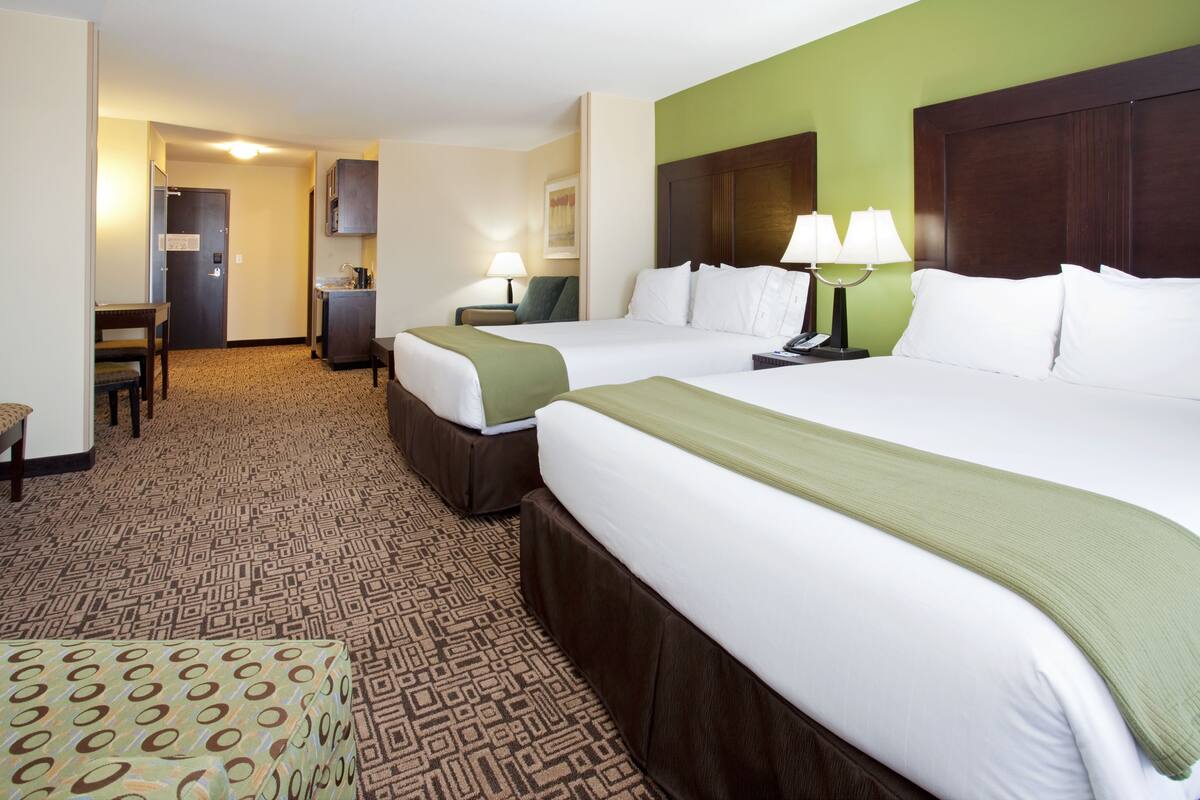 A hotel room with two beds, a desk, a chair, and a patterned carpet.