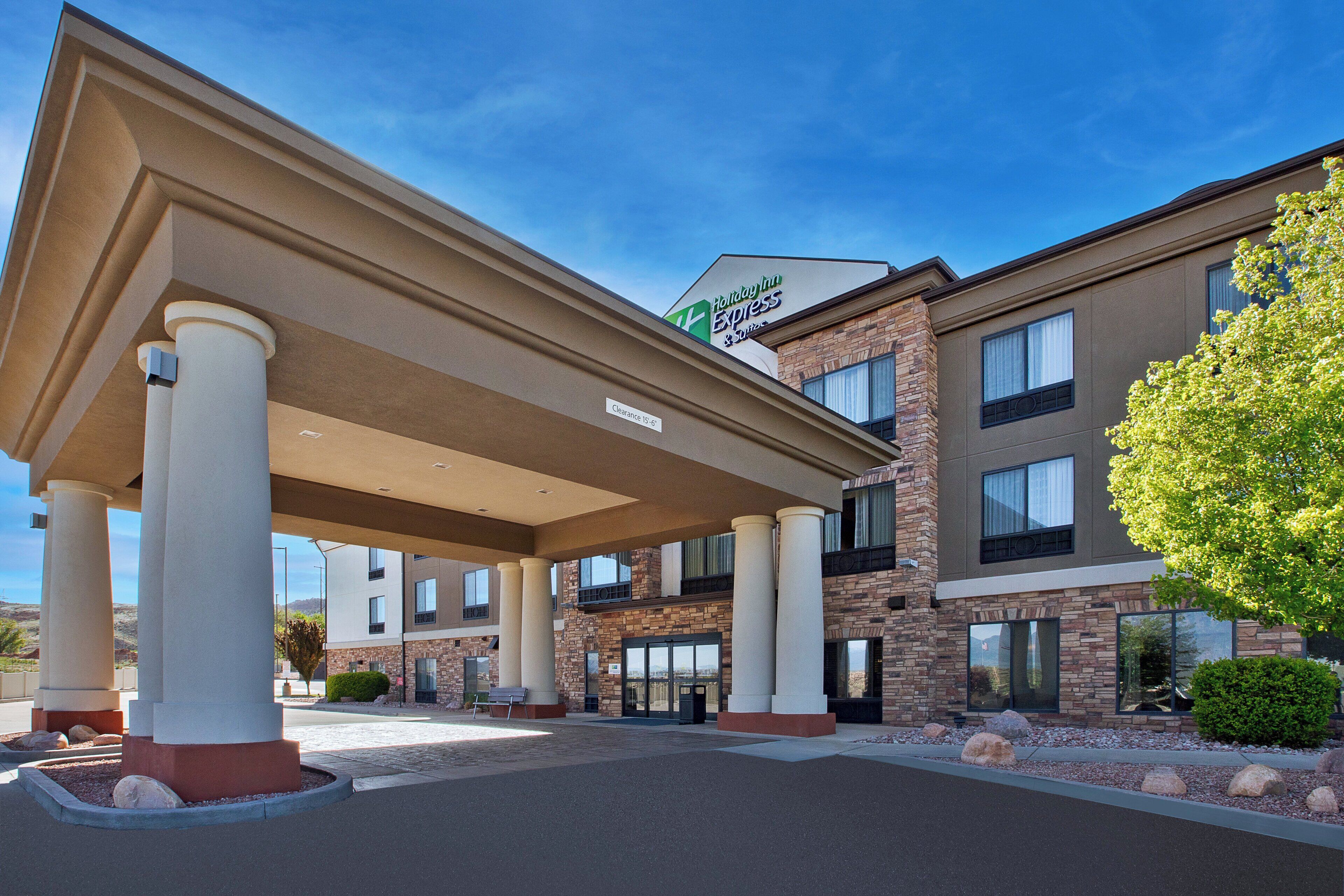 A Holiday Inn Express & Suites building with a covered entrance, stone facade, and a clear sky.