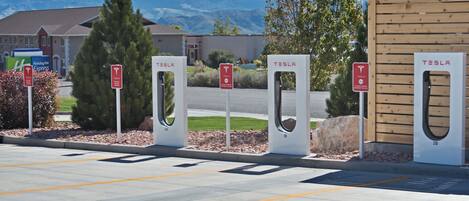 Un área de estacionamiento con varias estaciones de carga para Tesla, un letrero de Holiday Inn Express y un edificio al fondo.