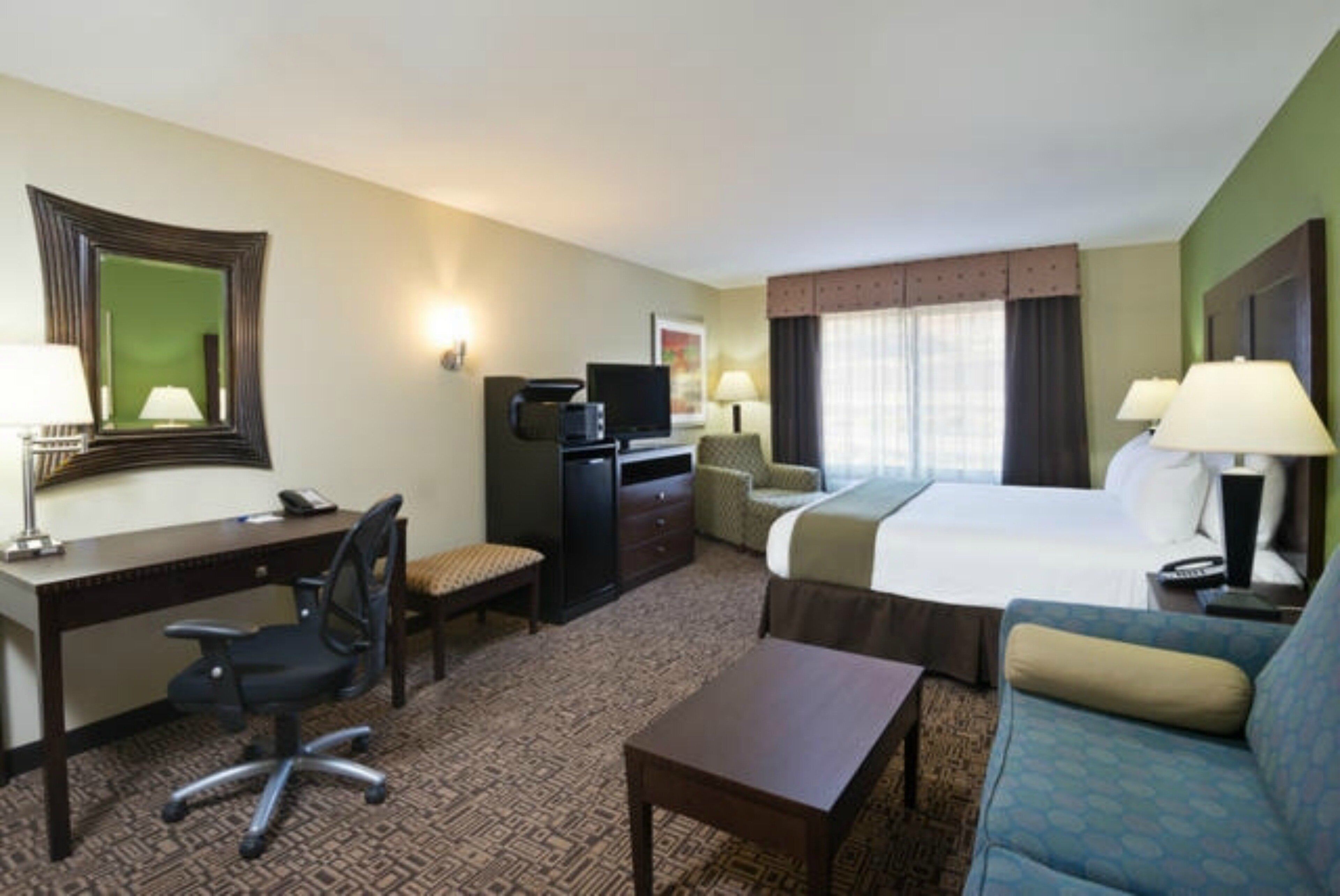 Una habitación de hotel con cama, escritorio, silla, televisor y sofá.