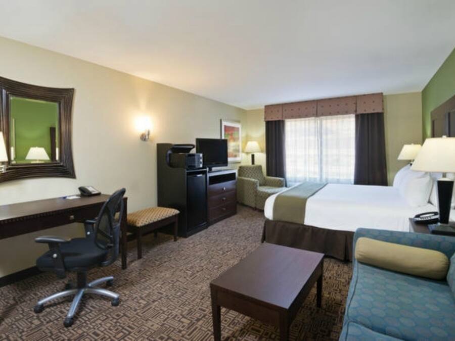 Una habitación de hotel con cama, escritorio, silla, televisor y sofá.