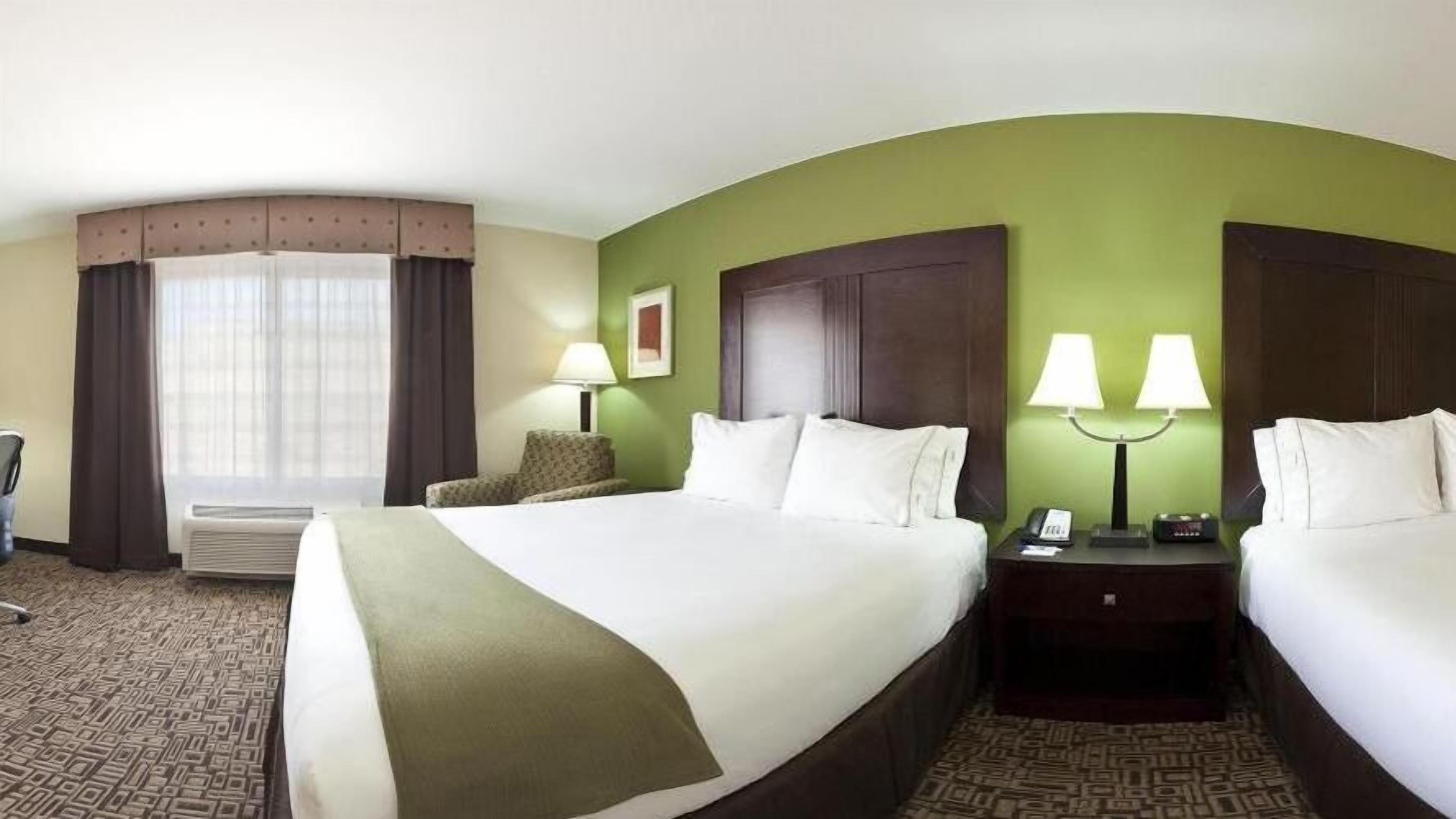 Une chambre d’hôtel avec un grand lit, deux tables de chevet avec des lampes, une chaise et une fenêtre avec des rideaux.