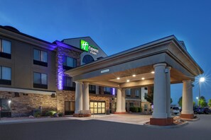 Un bâtiment de la chaîne Holiday Inn Express & Suites, doté d’une façade en pierre, de grandes colonnes et d’un espace d’entrée abrité.