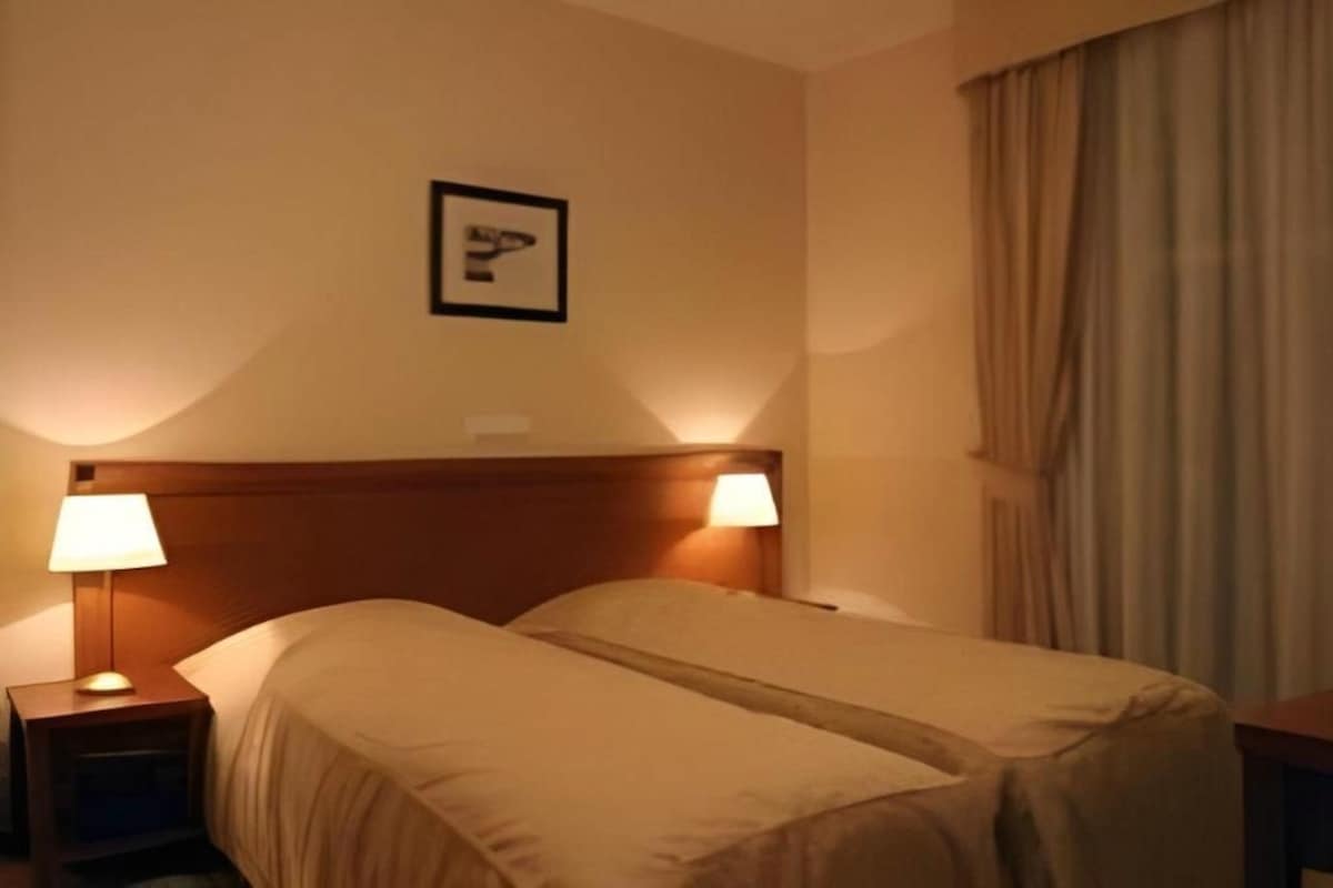 Una habitación de hotel con una cama doble, dos lámparas de noche, un cabecero y un cuadro en la pared.