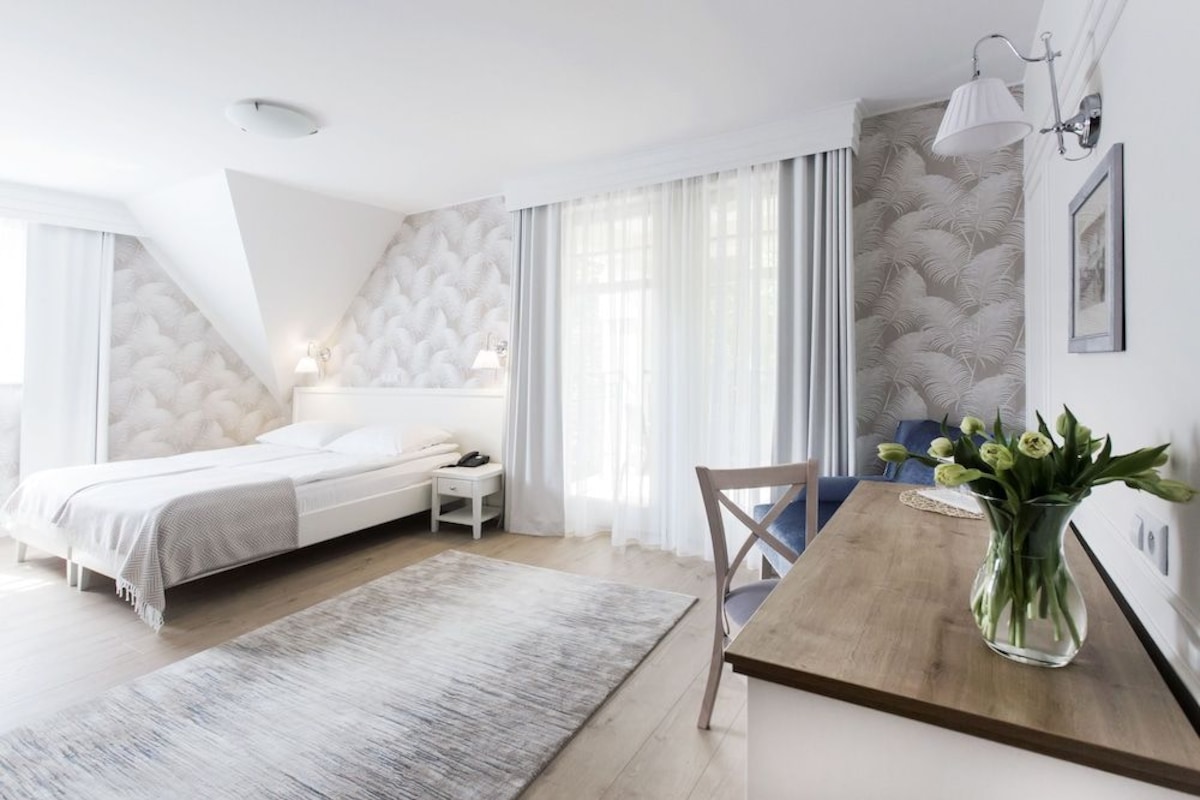 Un dormitorio moderno con cama, mesita de noche y velador. Se observa una mesa de madera con un florero.