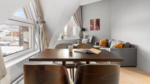 Un loft moderno con zona de comedor, un sofá gris y un amplio ventanal con vistas a la ciudad.