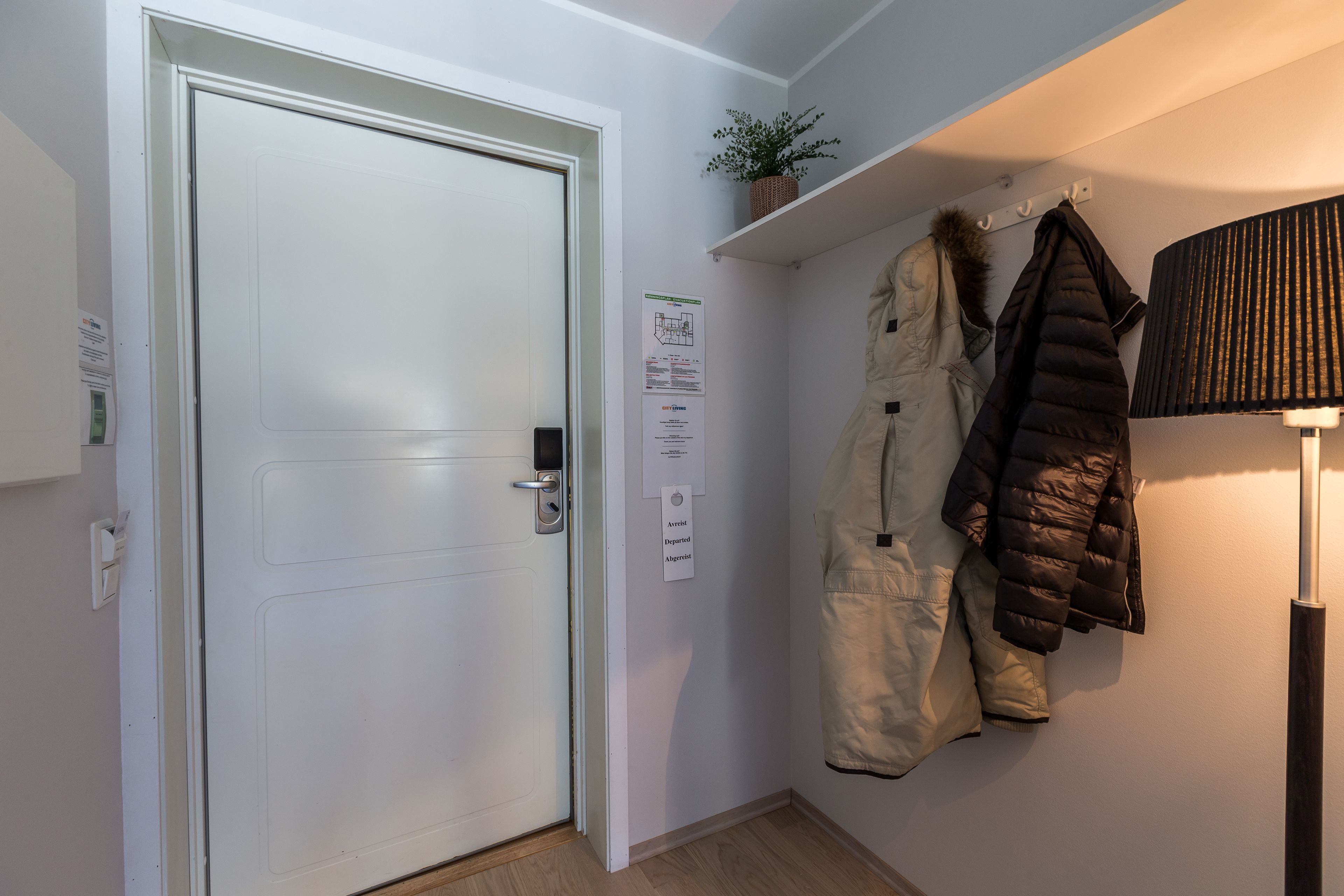 A hallway with a closed door, a wall-mounted coat rack with winter jackets, and a small potted plant.