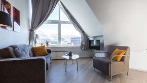 Una sala de estar moderna con un sofá, un sillón y una mesita. Un ventanal con cortinas ofrece vistas a un paisaje nevado.