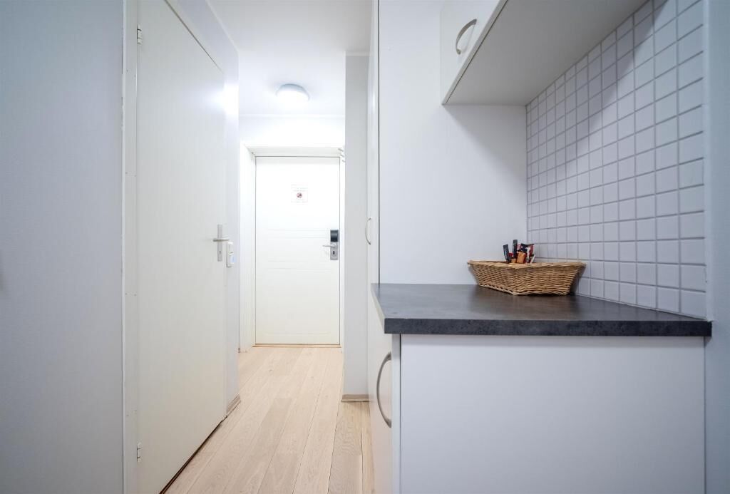 A narrow hallway with a kitchen area on the right, featuring a black countertop and a wicker basket.