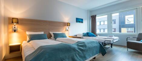 Habitación de hotel con dos camas, una mesita de noche, una silla y una ventana con cortinas.