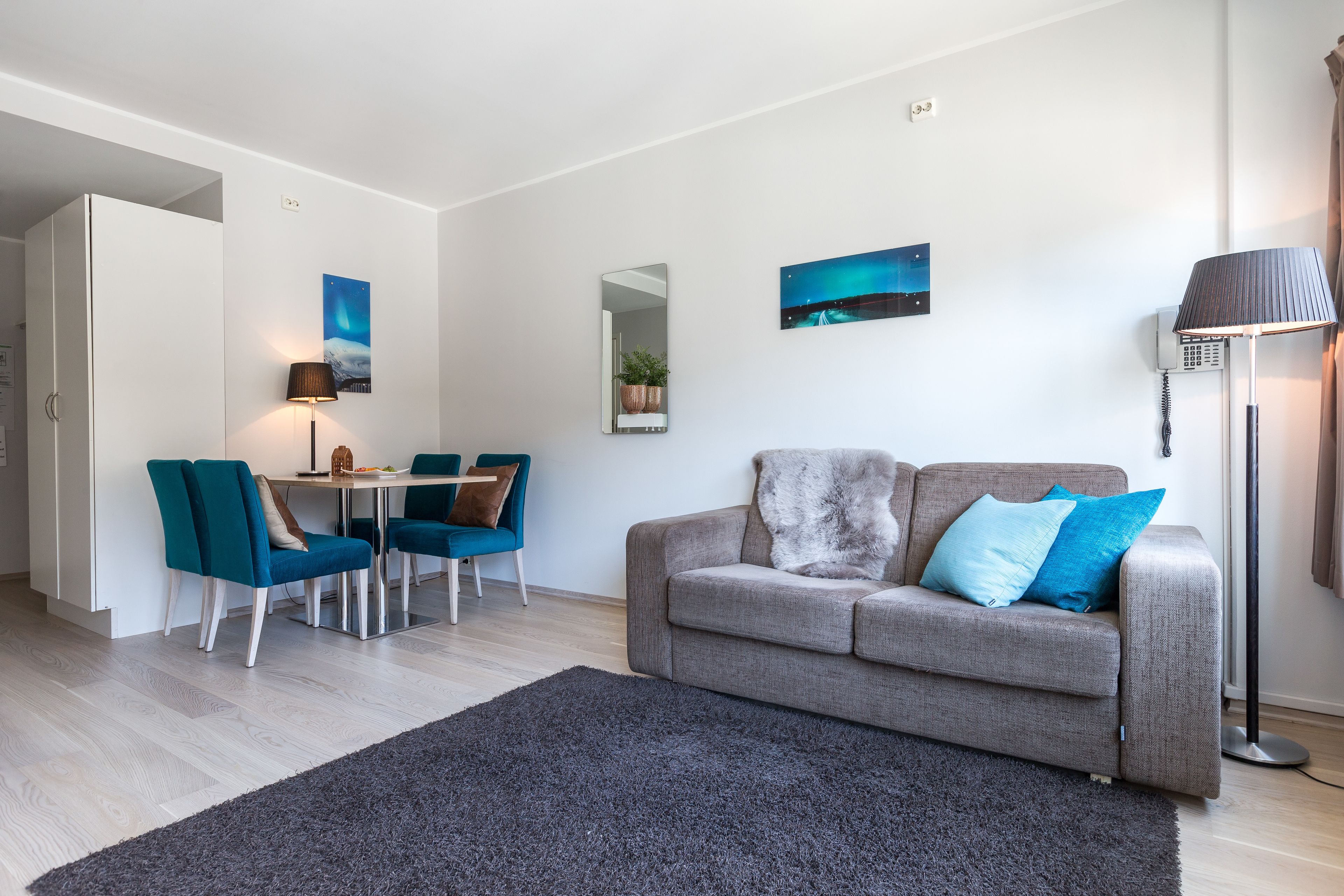 Un salon moderne avec un canapé gris, des fauteuils turquoise, une table à manger et un grand miroir.
