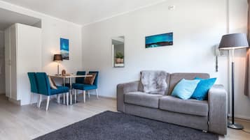 Un salon moderne avec un canapé gris, des fauteuils turquoise, une table à manger et un grand miroir.
