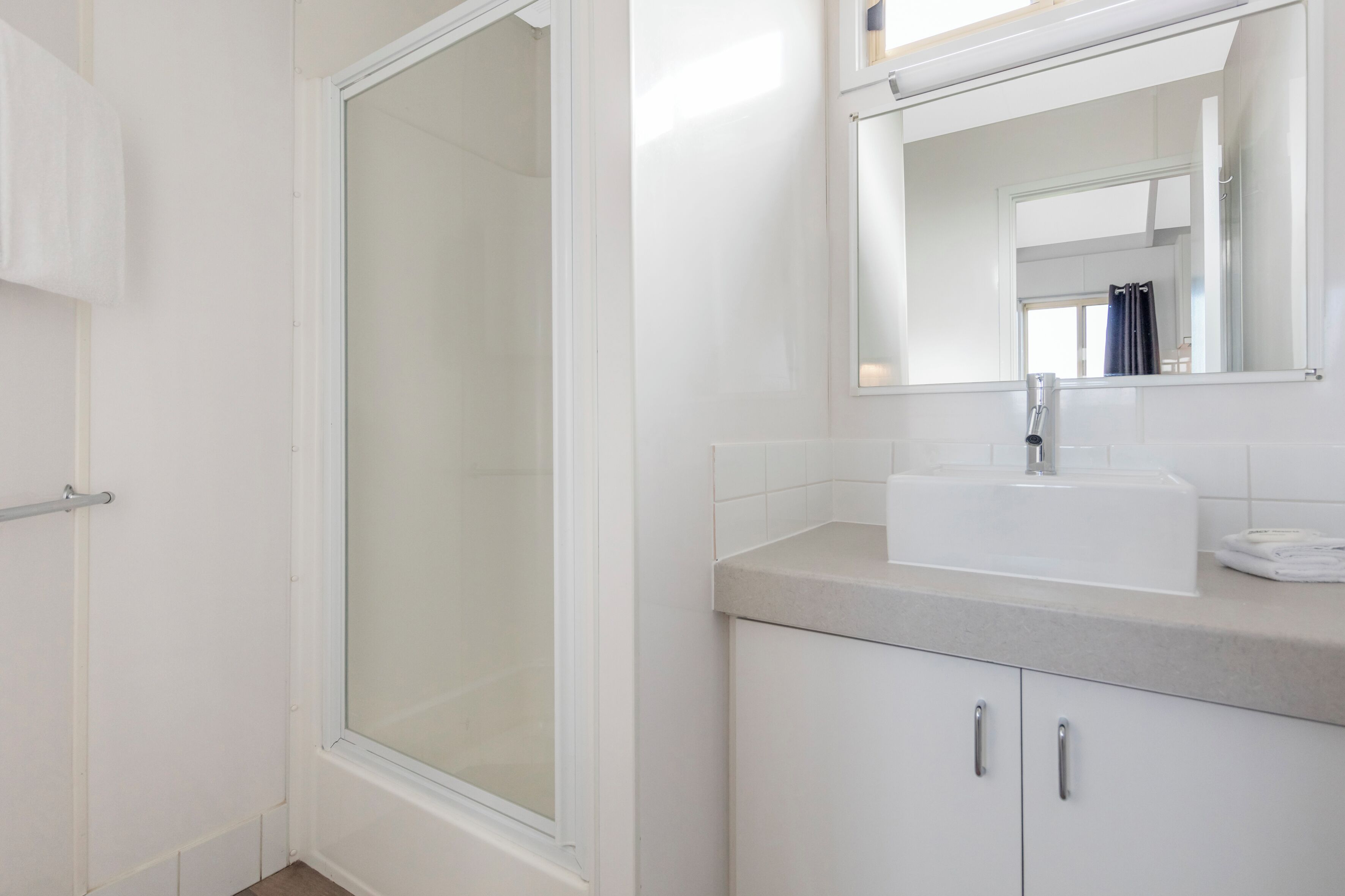 A bathroom with a glass shower enclosure, a white sink, and a mirror above it.
