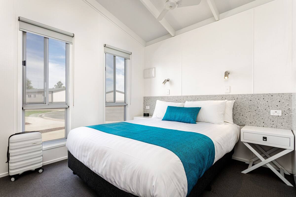 A hotel room with a large bed, a nightstand, a suitcase, and a window with a view of the outside.