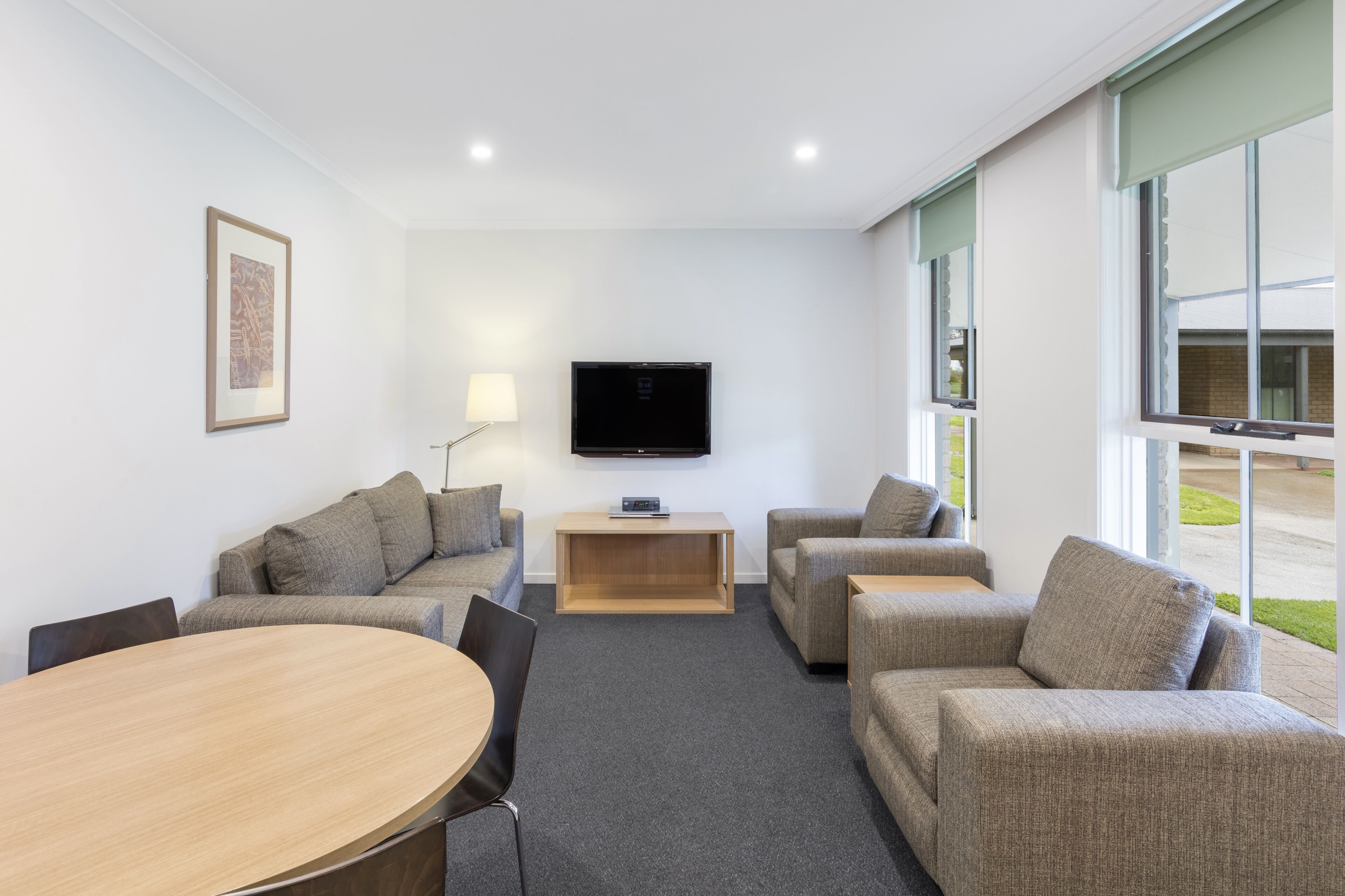 Ein modernes Wohnzimmer mit Flachbildfernseher, grauen Sofas, einem Holztisch und einem Esstisch.