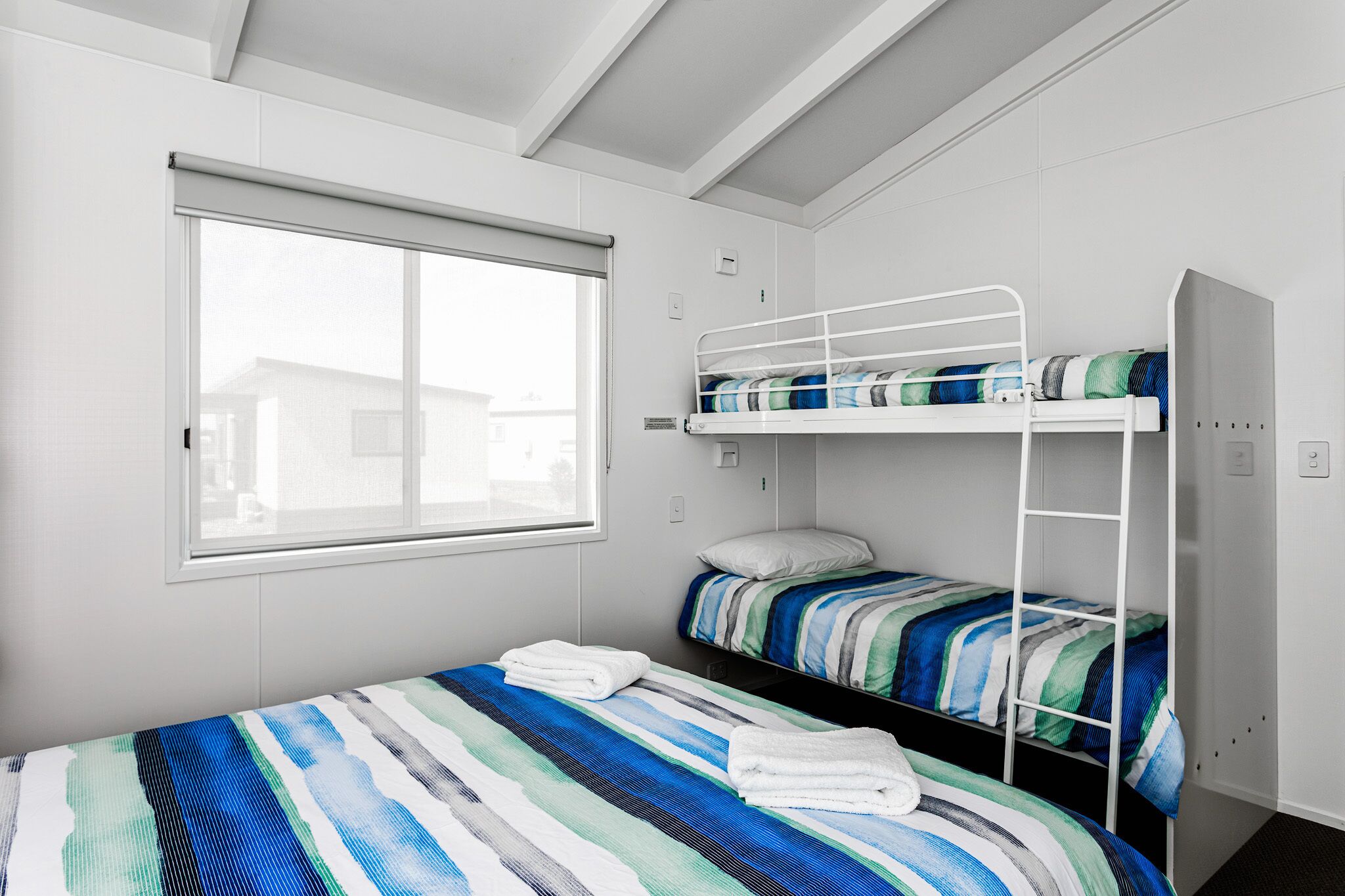 Habitación con literas, una ventana, ropa de cama a rayas y un armario blanco.