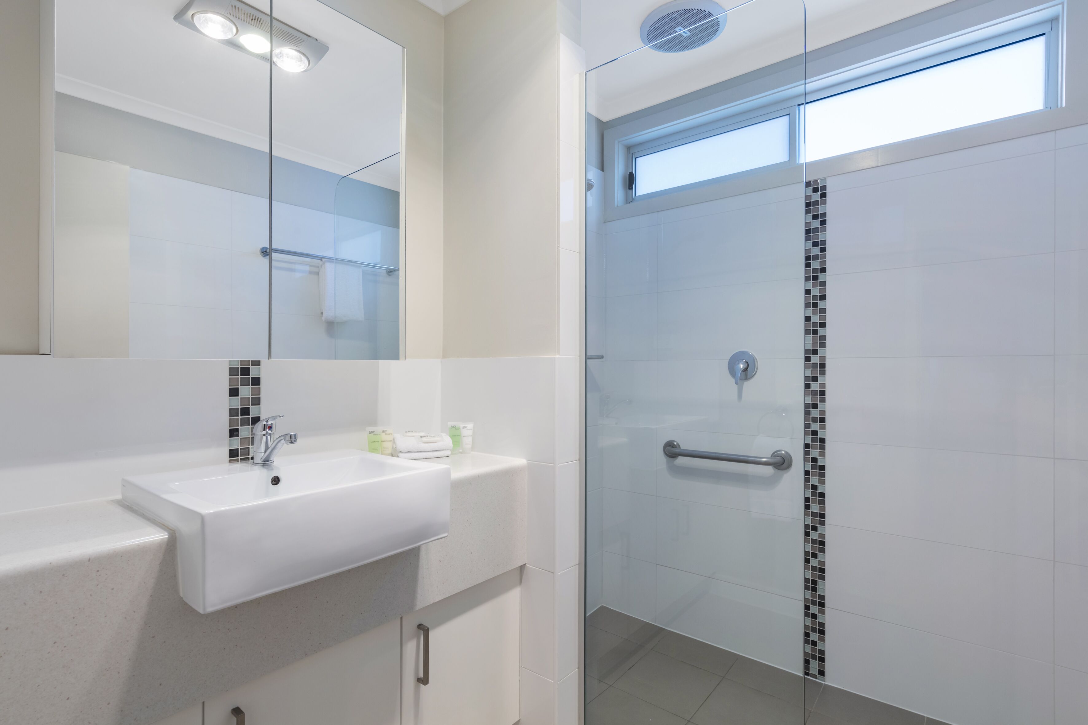 A modern bathroom with a glass shower door, a white sink, and a mirror above it.