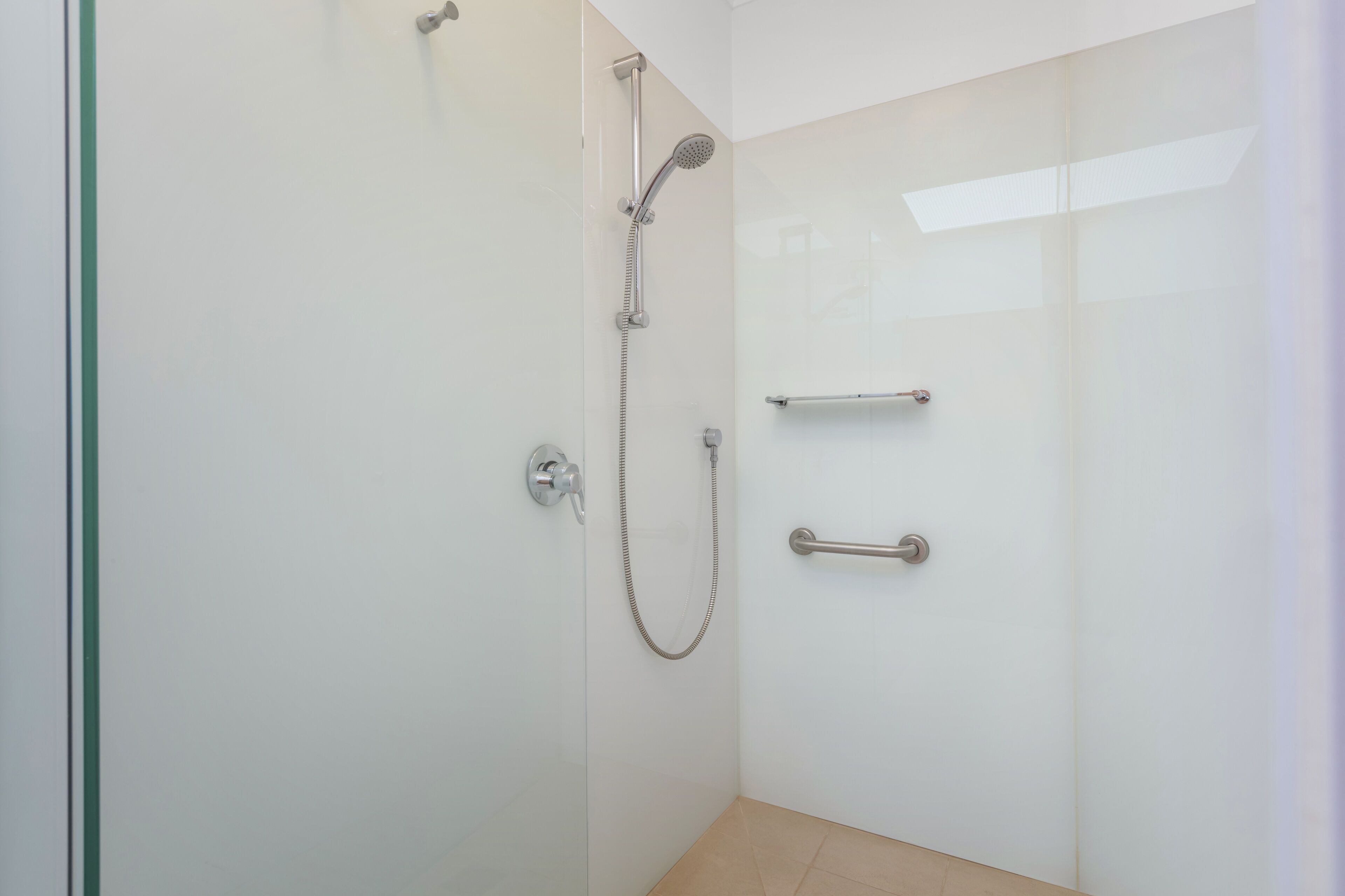 Un baño moderno con cabina de ducha de vidrio, ducha de mano y un perchero para toallas.