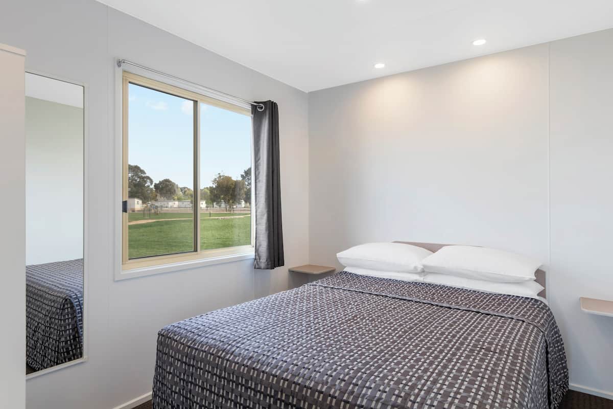 A modern bedroom with a large bed, a window with a view of a park, and a mirror on the wall.
