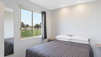 Une chambre moderne avec un grand lit, une fenêtre donnant sur un parc et un miroir au mur.