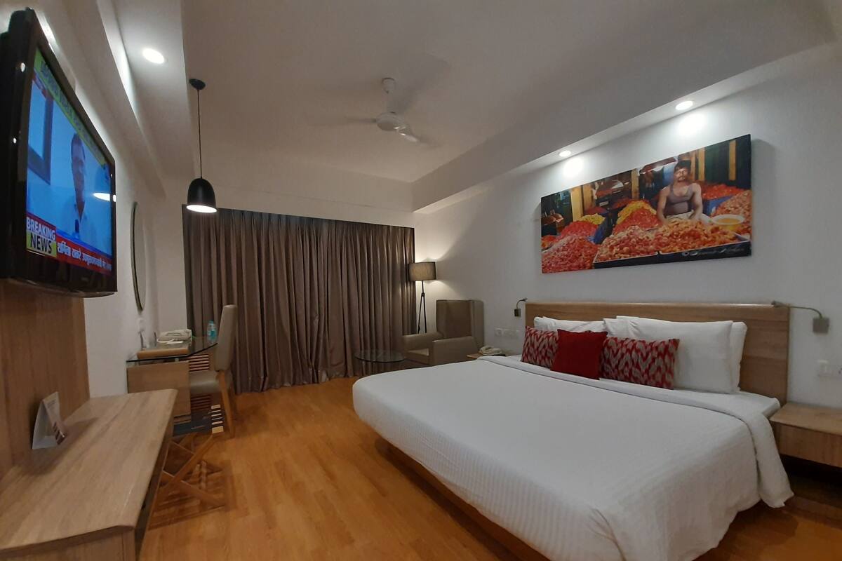A hotel room with a large bed, a flat-screen TV, a desk, and a ceiling fan.