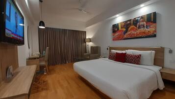 A hotel room with a large bed, a flat-screen TV, a desk, and a ceiling fan.
