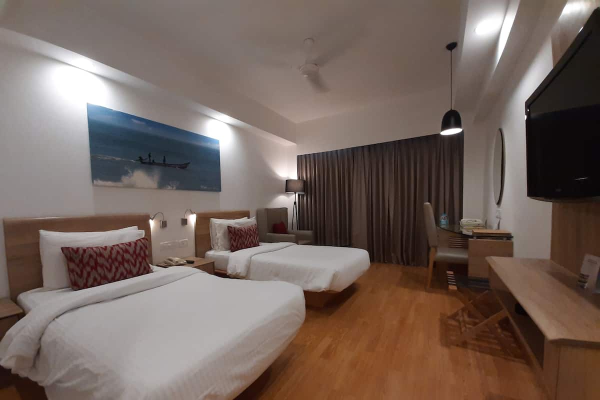 A hotel room with two beds, a desk, a chair, a TV, a painting, and a ceiling fan.