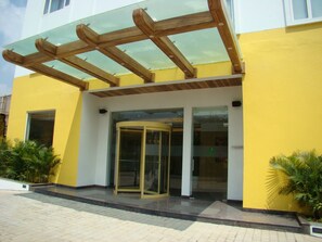A building with a yellow exterior, a glass entrance, and a wooden pergola above the entrance.