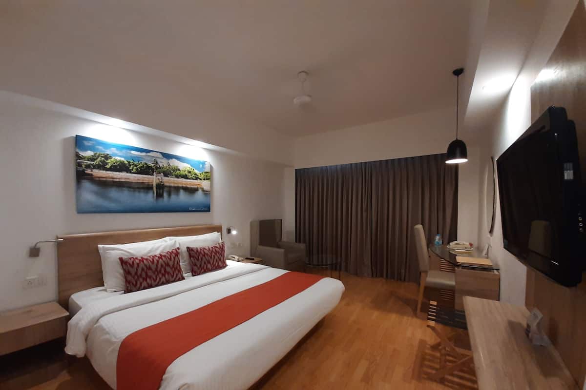 A hotel room with a large bed, a desk with a chair, a flat-screen TV, and a painting of a landscape on the wall.
