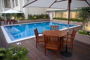 A wooden deck with a pool table and chairs, surrounded by a swimming pool.