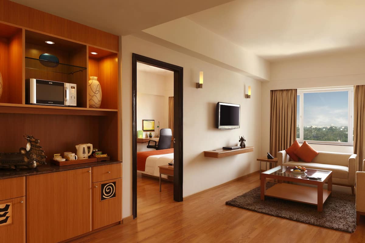 A modern hotel room with a wooden cabinet, a flat-screen TV, a sofa, and a coffee table.
