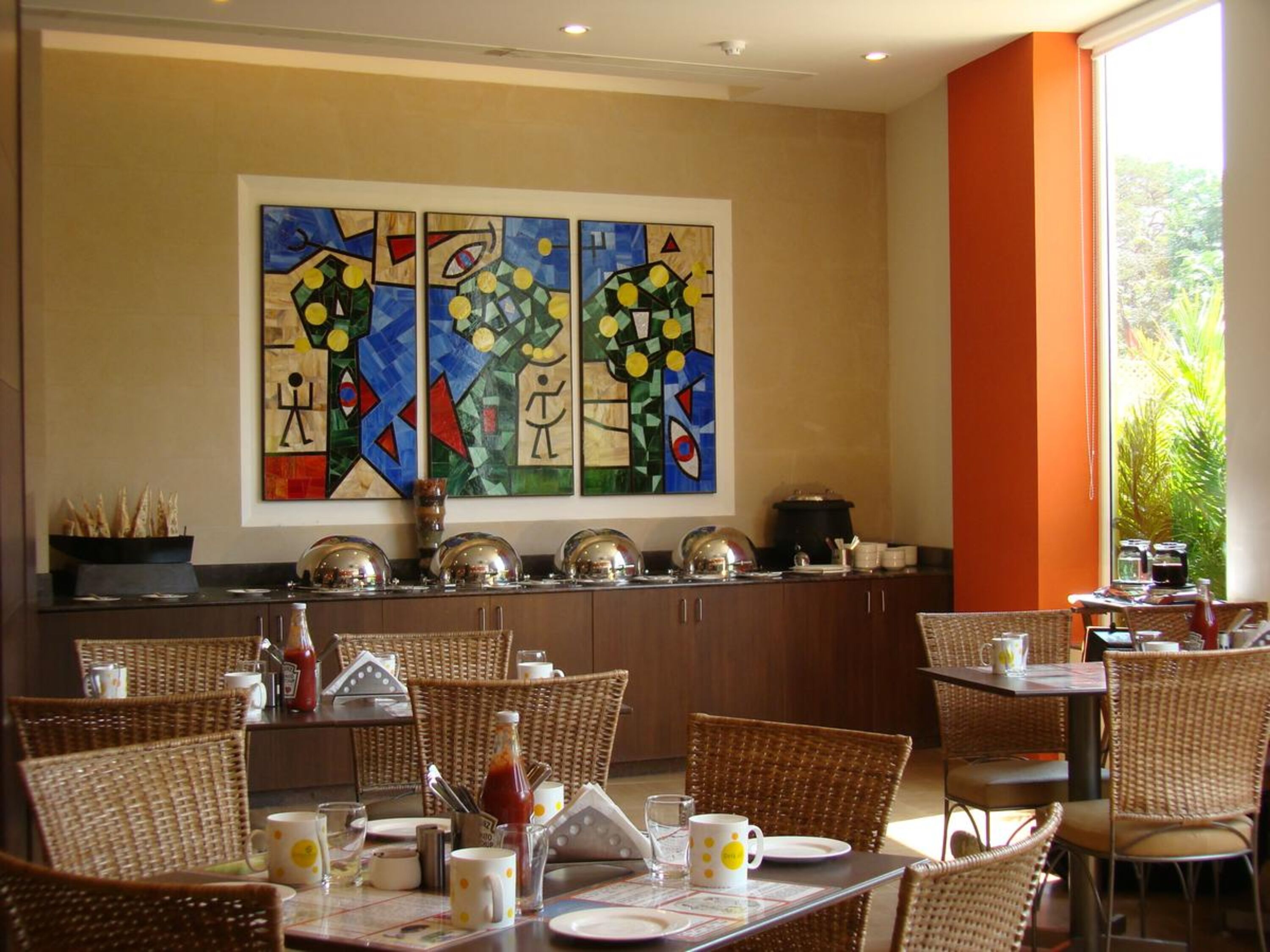 A dining area with wicker chairs, a buffet setup, and abstract art on the wall.