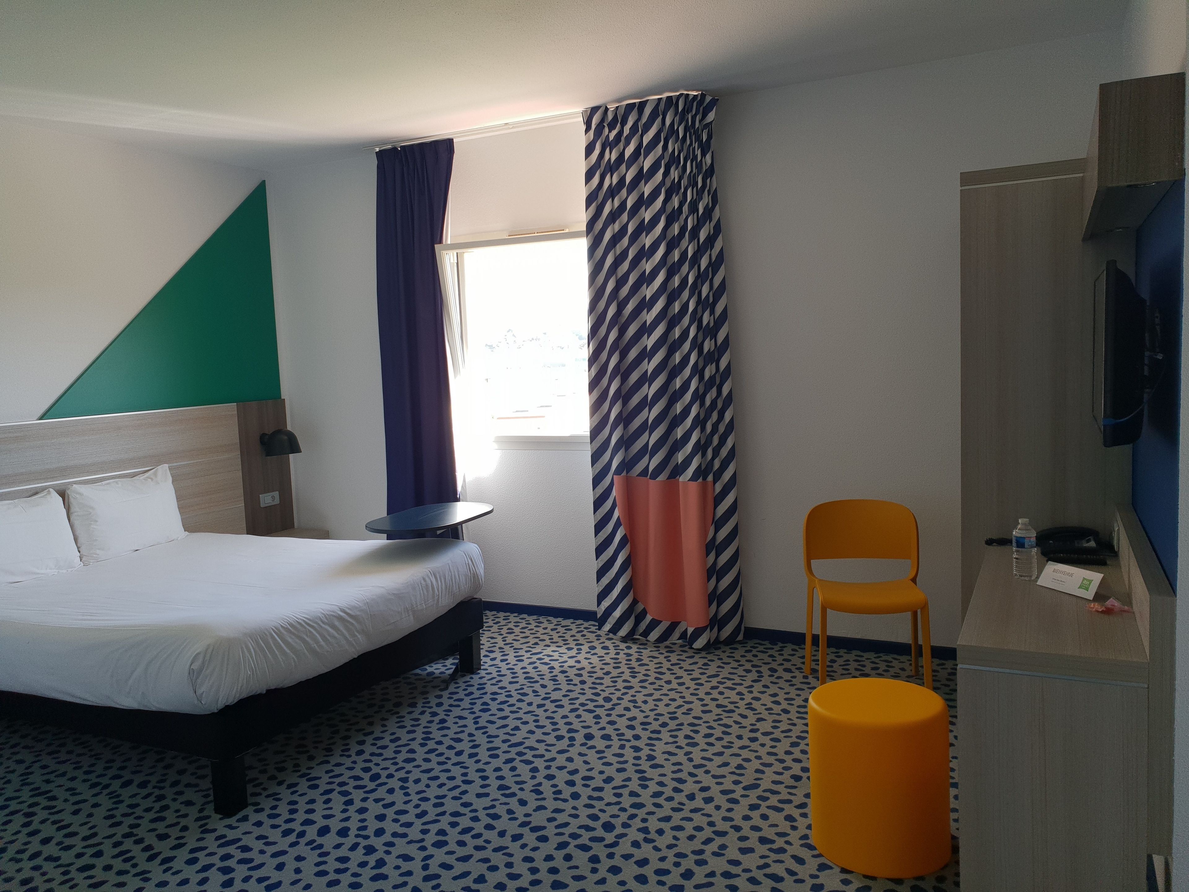 A hotel room with a bed, a desk, a chair, and a television.