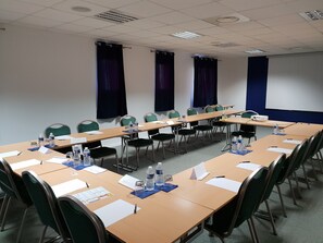 Un salón de conferencias con largas mesas, sillas, tarjetas de identificación, botellas de agua y una pantalla de proyector.