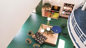 An indoor space with a green floor, wooden furniture, and a circular seating area with a blue table.