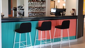 A bar area with a counter, three black bar stools, and shelves with bottles and glasses. - ibis Styles Marseille Plan de Campagne (Les Pennes-Mirabeau)