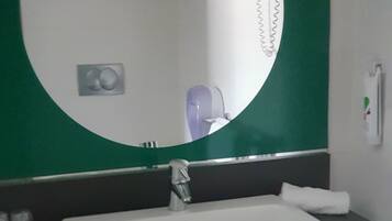 Un baño con un lavabo blanco, un espejo redondo y una pared verde.