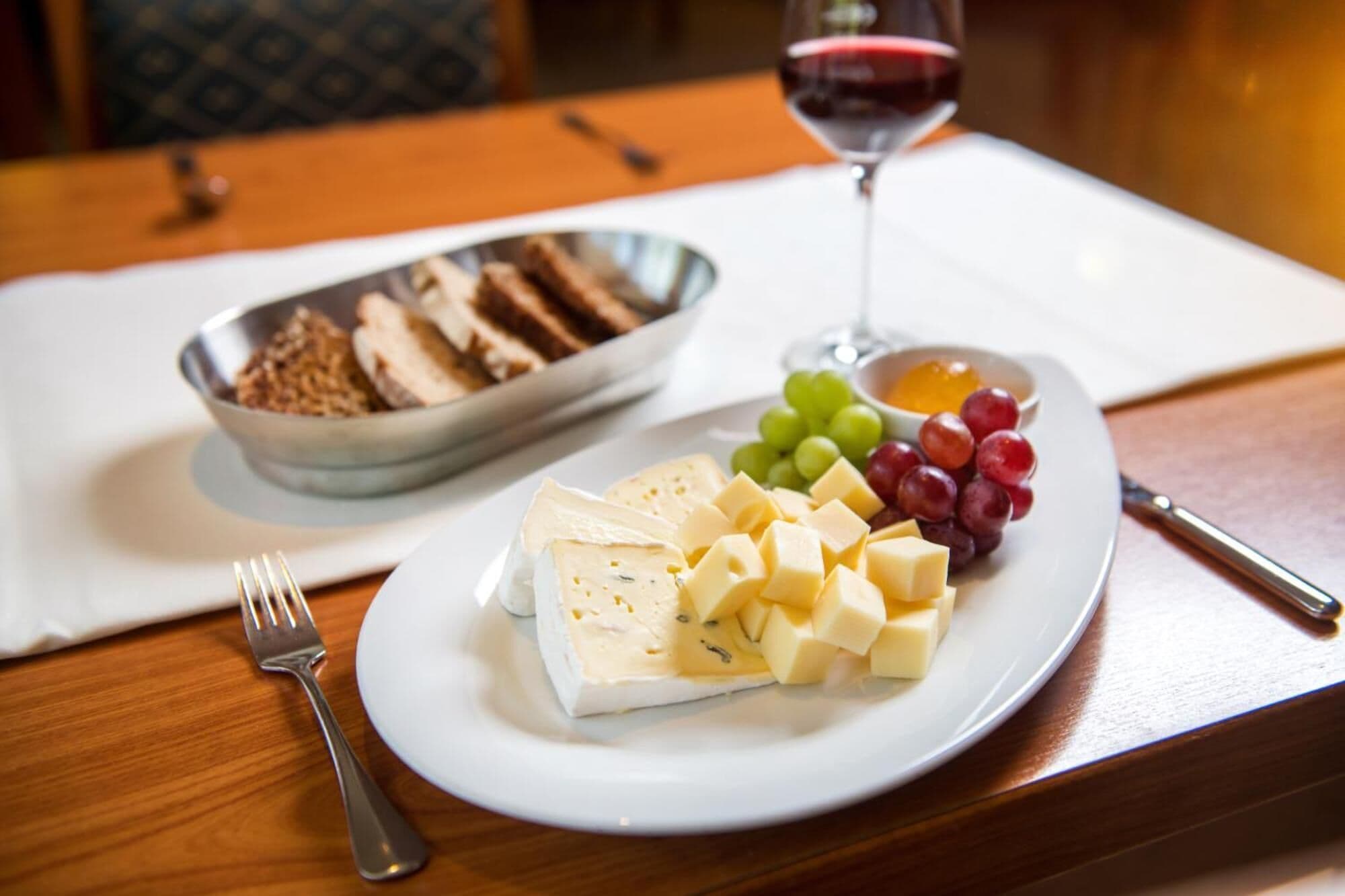 A plate with cheese, grapes, and a bowl of bread on a wooden table.