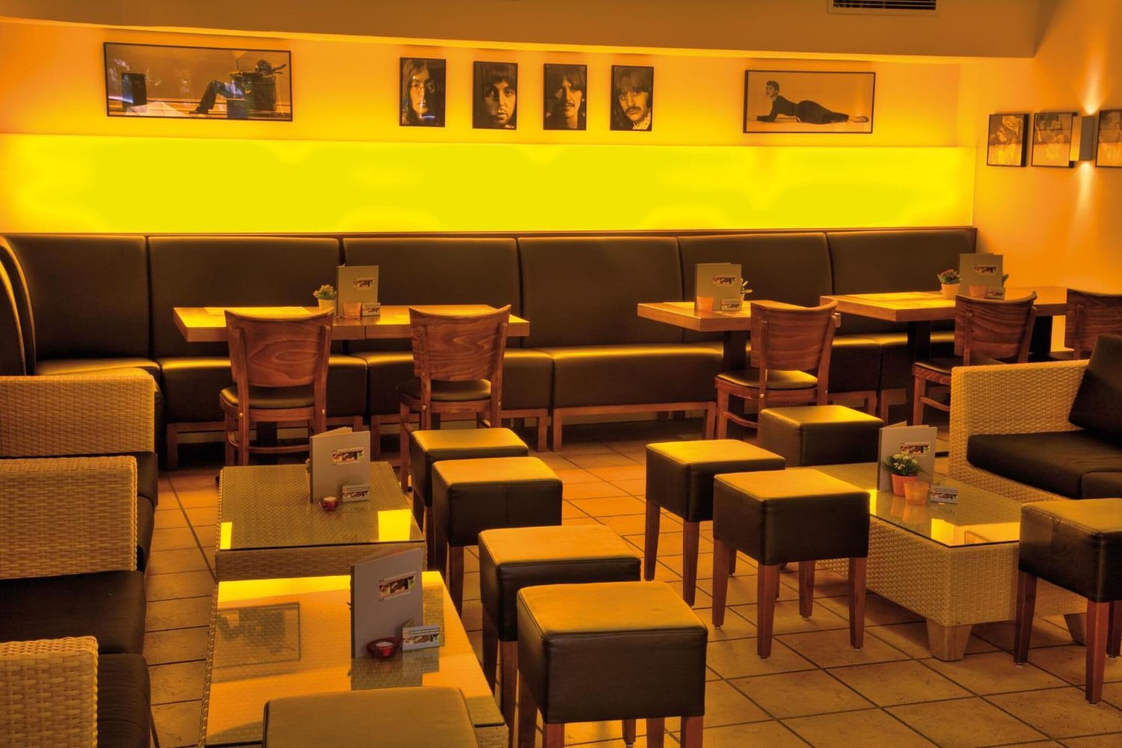 A restaurant with a warm yellow lighting, black leather seating, and framed pictures on the wall.