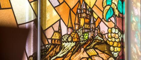 Una ventana de vitral con una representación detallada de un castillo y el paisaje circundante.