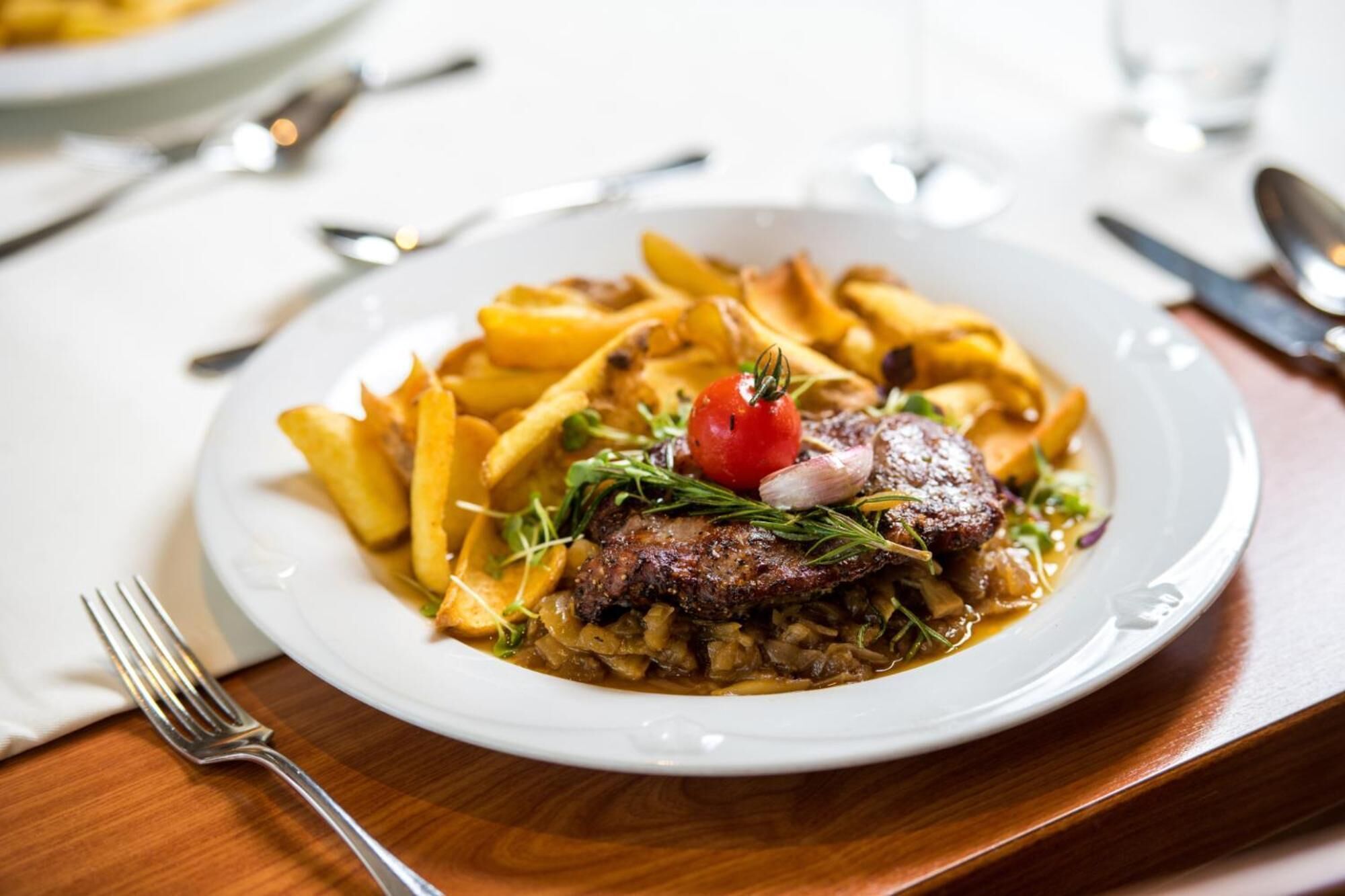 Un plato de comida con papas fritas, un bistec y un tomate cherry sobre un plato blanco.