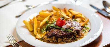 A plate of food with fries, a steak, and a cherry tomato on a white plate.